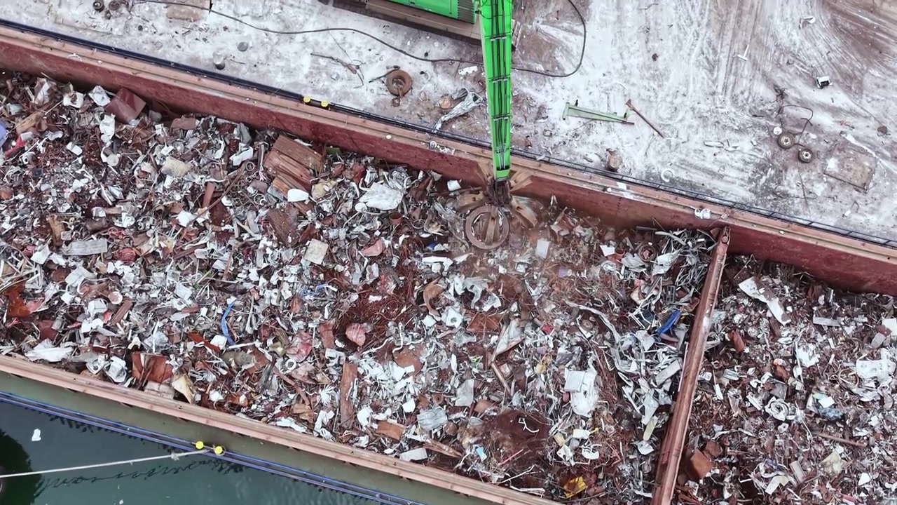 Operai rimuovono detriti metallici dall'acqua utilizzando macchinari pesanti in un molo vicino a una città durante il giorno in una trafficata area industriale