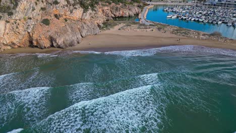 Waves-hitting-a-rocky-beach-near-a-harbor-in-ginesta,-barcelona,-aerial-view