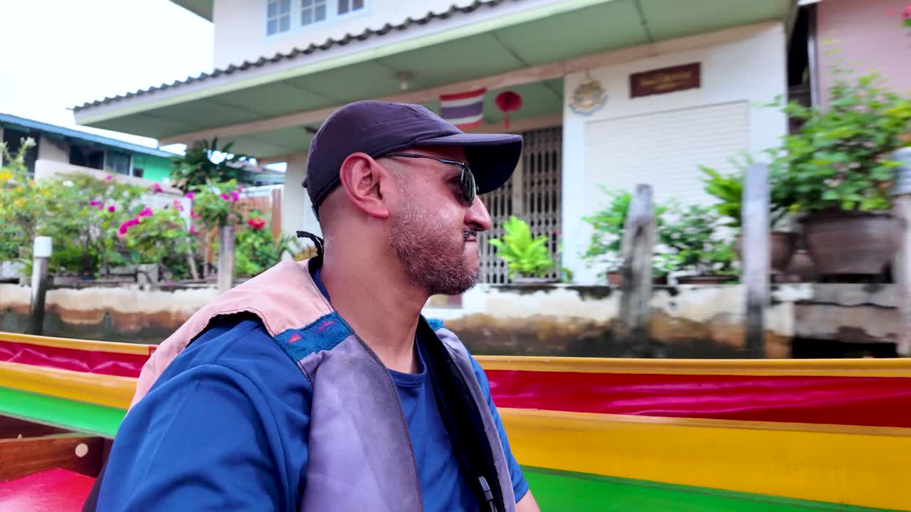 Man wearing sunglasses and a cap enjoying a long tail boat ride in Bangkok