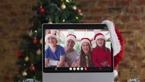 Happy-family-wearing-santa-hats-on-laptop-video-call,-with-christmas-decorations-and-tree