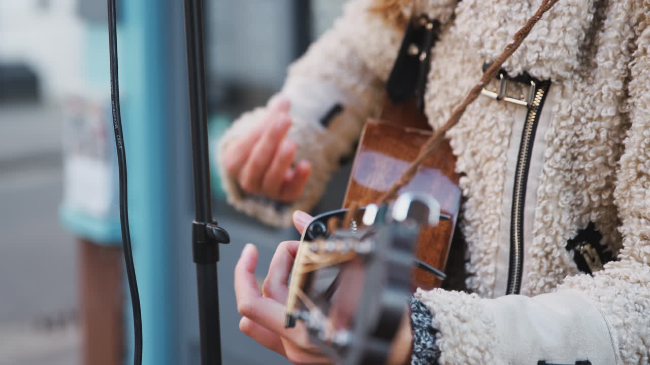 close up de una músico femenina tocando la guitarra acústica al aire libre en la calle