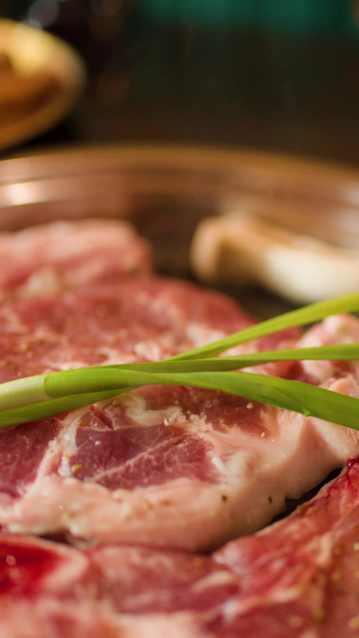 Carne di manzo marmorizzata cruda e cipollotto verde che sfrigolano su una padella grill rovente, con vapore che sale, messa a fuoco ridotta