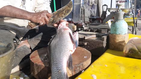 puesto en el mercado de pescado de marisco indio con trozos masculinos de salmón crudo recién capturado con un gran cuchillo de metal en una mesa de cerca con fondo borroso