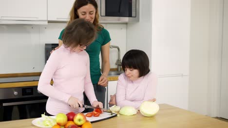 Zwei-Mädchen-Mit-Down-Syndrom-Schneiden-Mit-Ihrer-Mutter-In-Der-Küche-Gemüse