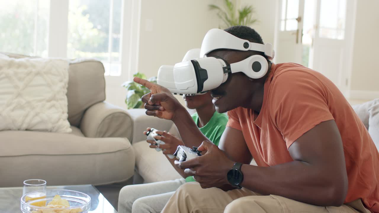 Un gioco VR appena iniziato fa sì che padre e figlio si sporgano in avanti, indicando qualcosa sul divano mentre tengono i gamepad.