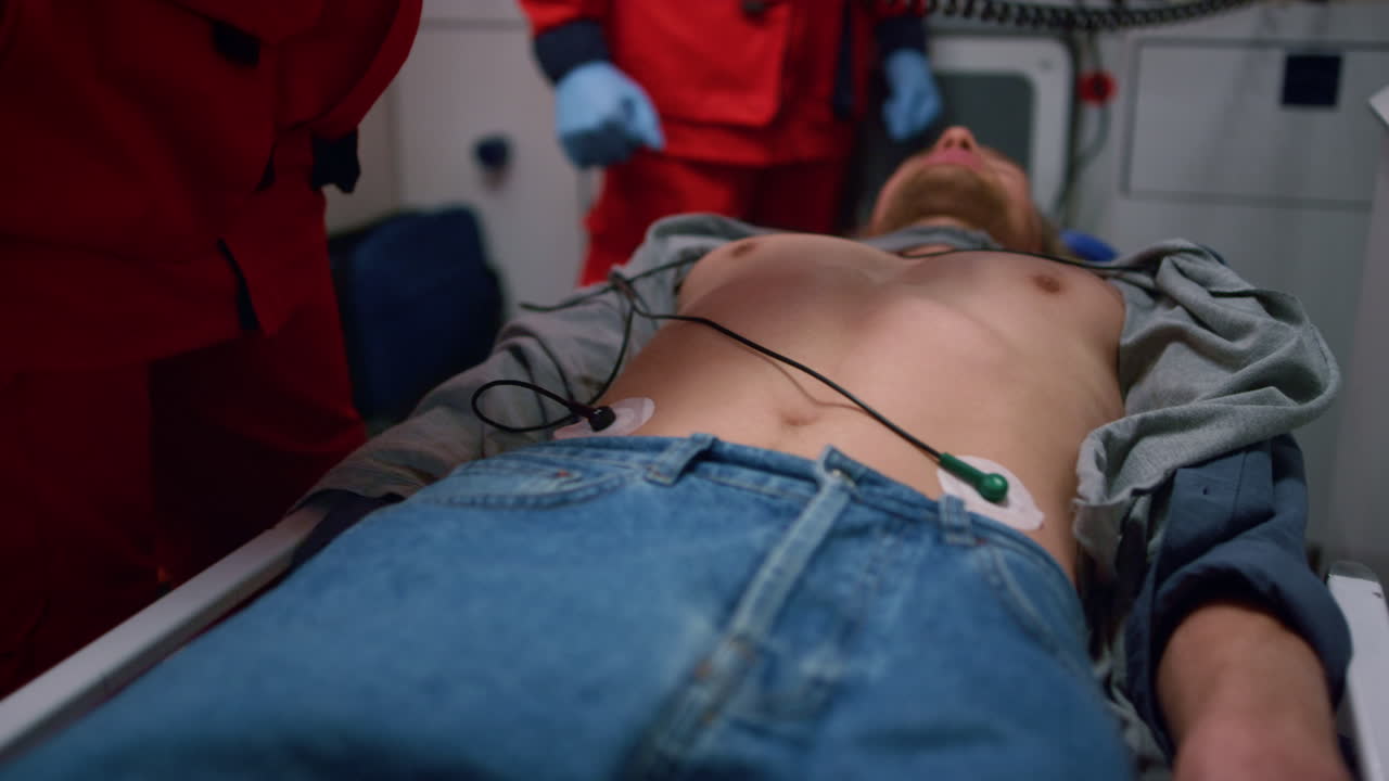 응급차에 있는 남자에게 디피브릴레이터로 심폐소생술을 하는 구급대원들의 손