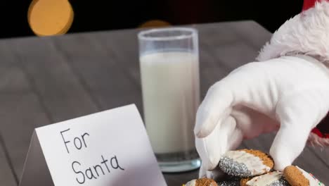 Animation-of-santa-claus-picking-cookies-over-orange-spots-of-light
