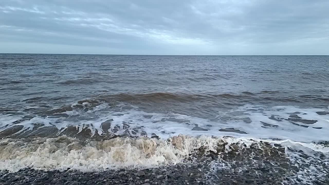sucias ondas de marea en cámara lenta chocando contra la tempestuosa orilla de guijarros mirando hacia el horizonte