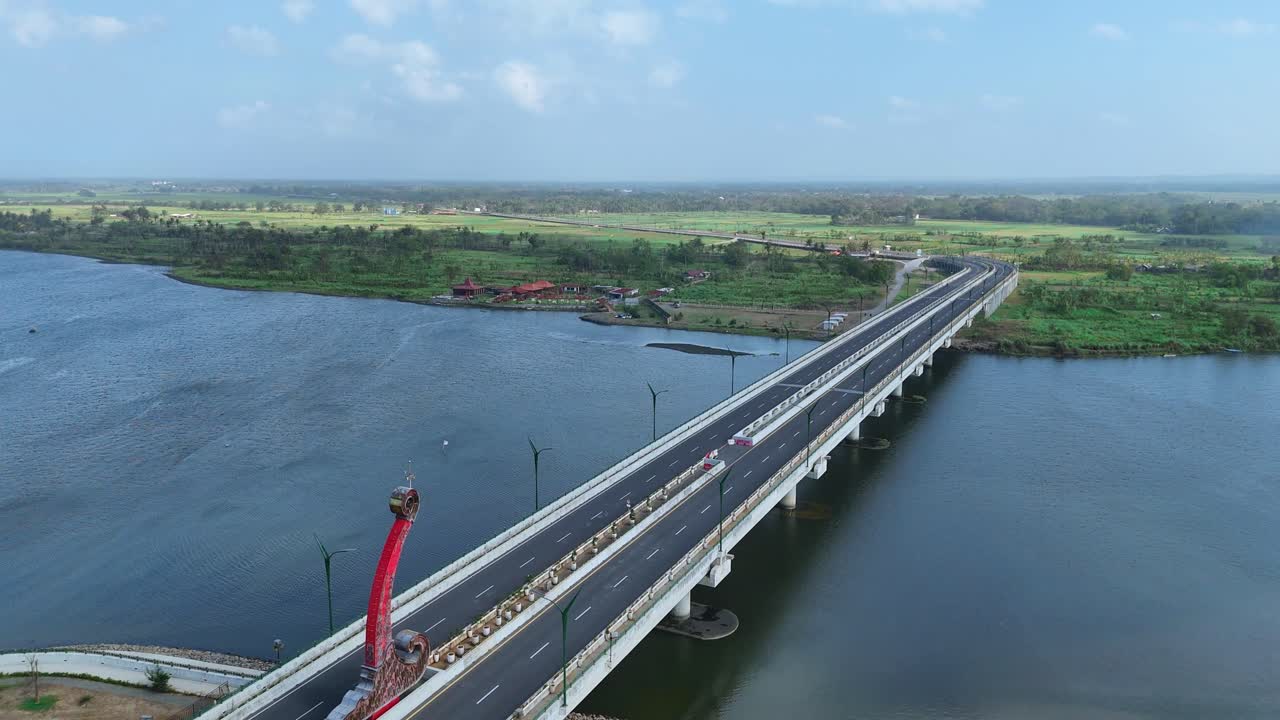 Aerial view of asphalt road on the bridge. Big bridge on the wide river and green rural landscape on the background. Blue sky on the horizon. 4K drone shot.