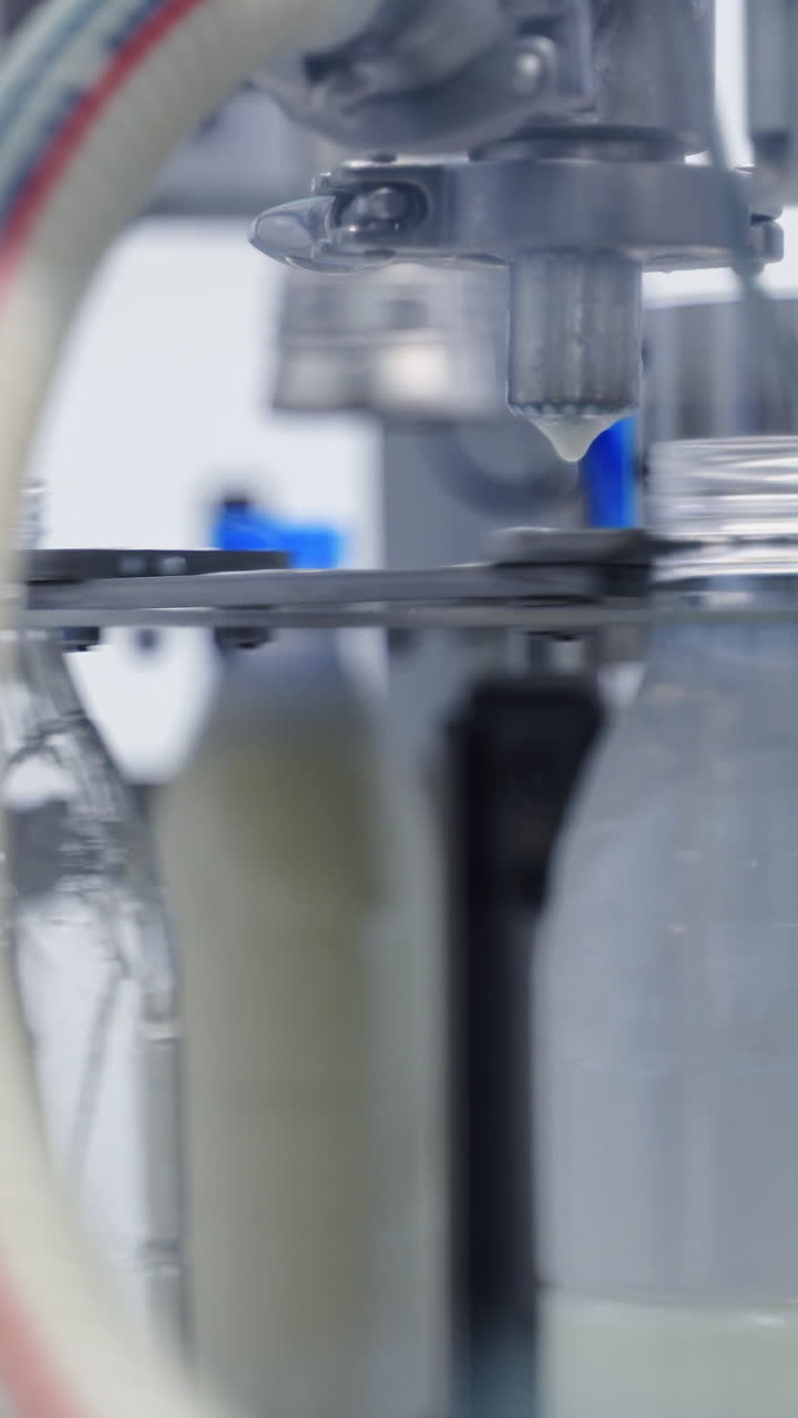 Automated technology of bottling milk in robotic factory. Plastic bottles are filling with milk by modern machinery at a dairy plant. Close-up. Vertical video