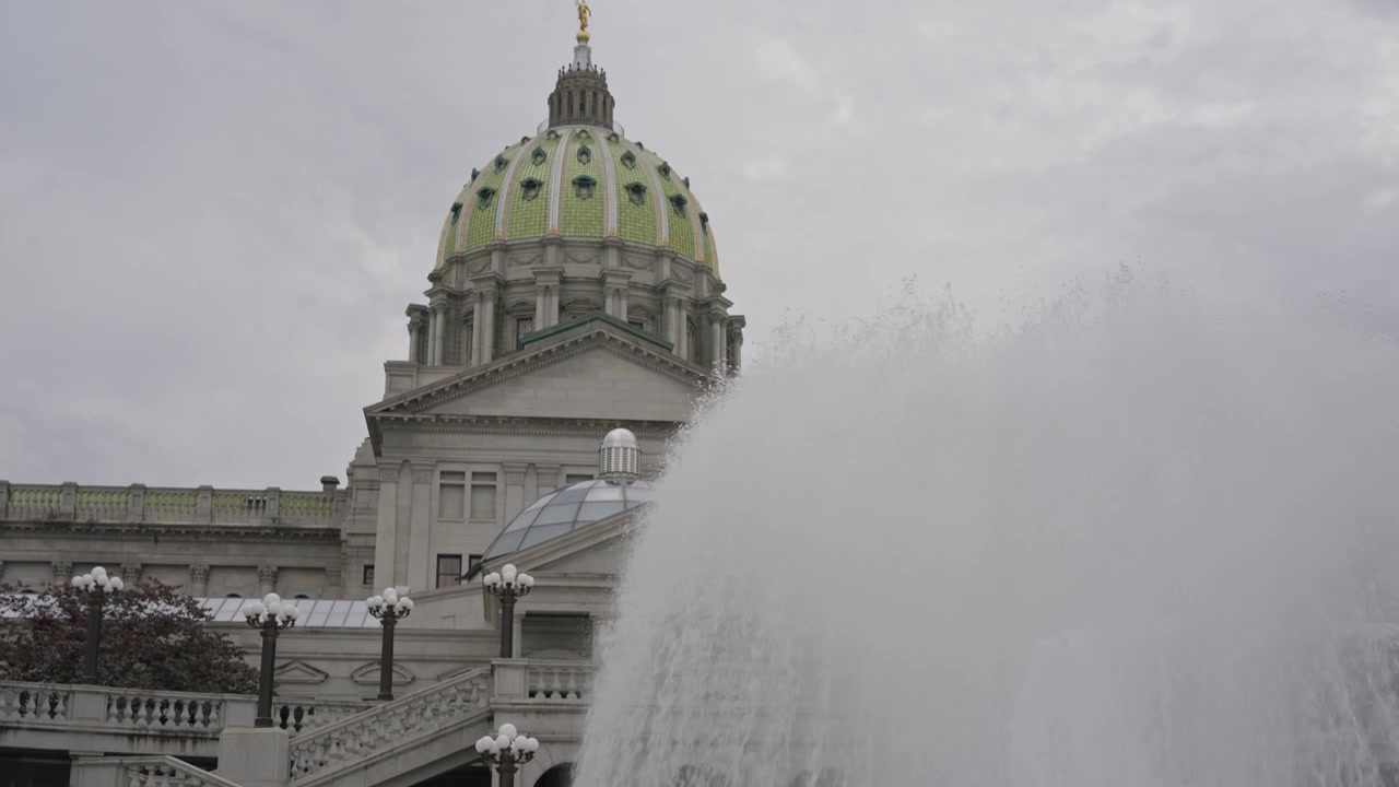 Una ripresa cinematografica con inclinazione verso l'alto e carrellata in avanti dalla fontana verso il Campidoglio dello Stato della Pennsylvania a Harrisburg, Pennsylvania, rivelando la storica architettura governativa e la grandezza civica.
