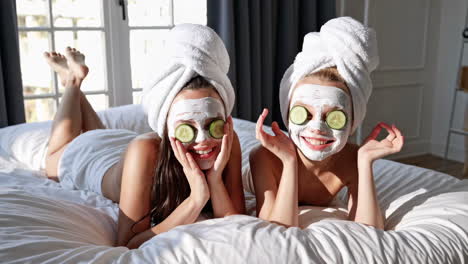 two girls enjoying a spa day with face masks and cucumber slices