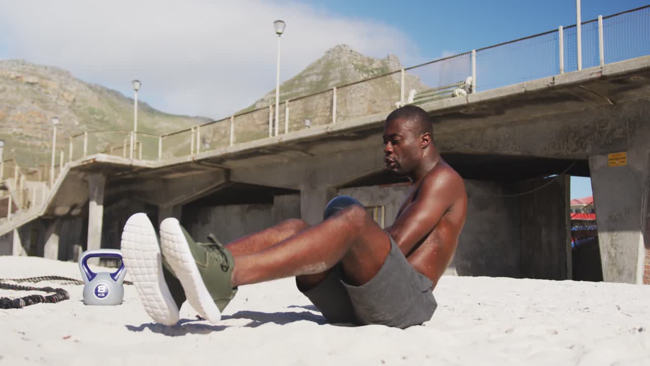 Fokuseret afroamerikansk mand laver vrid med bold og træner udendørs på stranden.