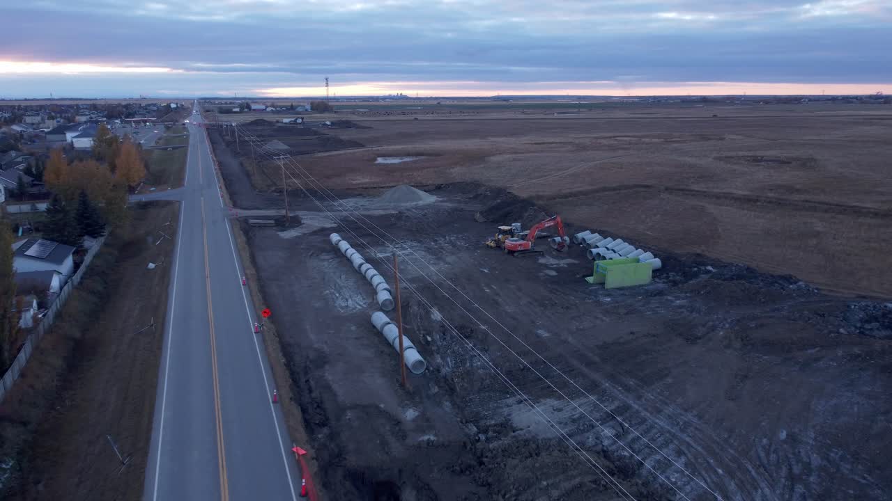 Construction machinery with pipes concrete by neighborhood road approached shot aerial evening