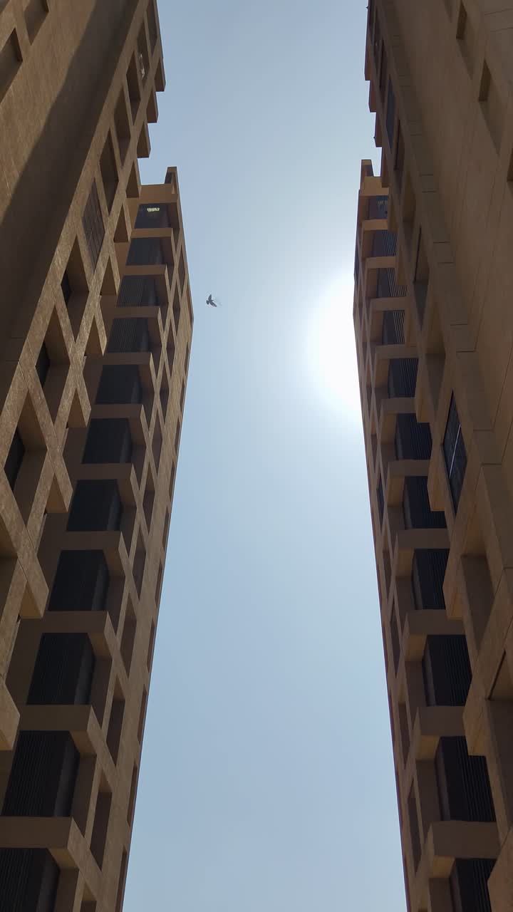 Vista vertical de dois edifícios modernos imponentes com o sol brilhando entre eles.