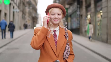 woman in beret and coat talking on phone in city street