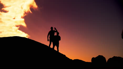 Silhouetted people reaching the summit at sunset