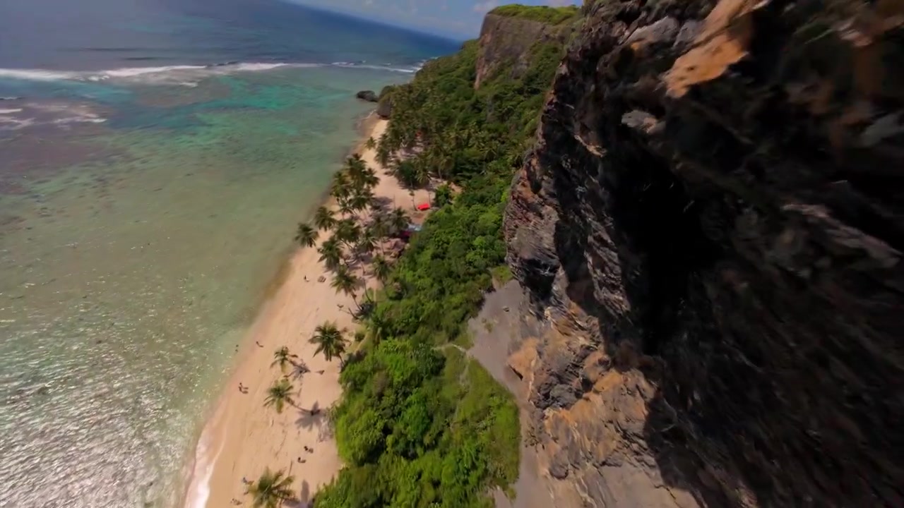 FPV-drone lentää kallionseinämää pitkin kohti syrjäistä trooppista Playa Frontonin rantaa Dominikaanisessa tasavallassa. Ilmakuva eteenpäin.