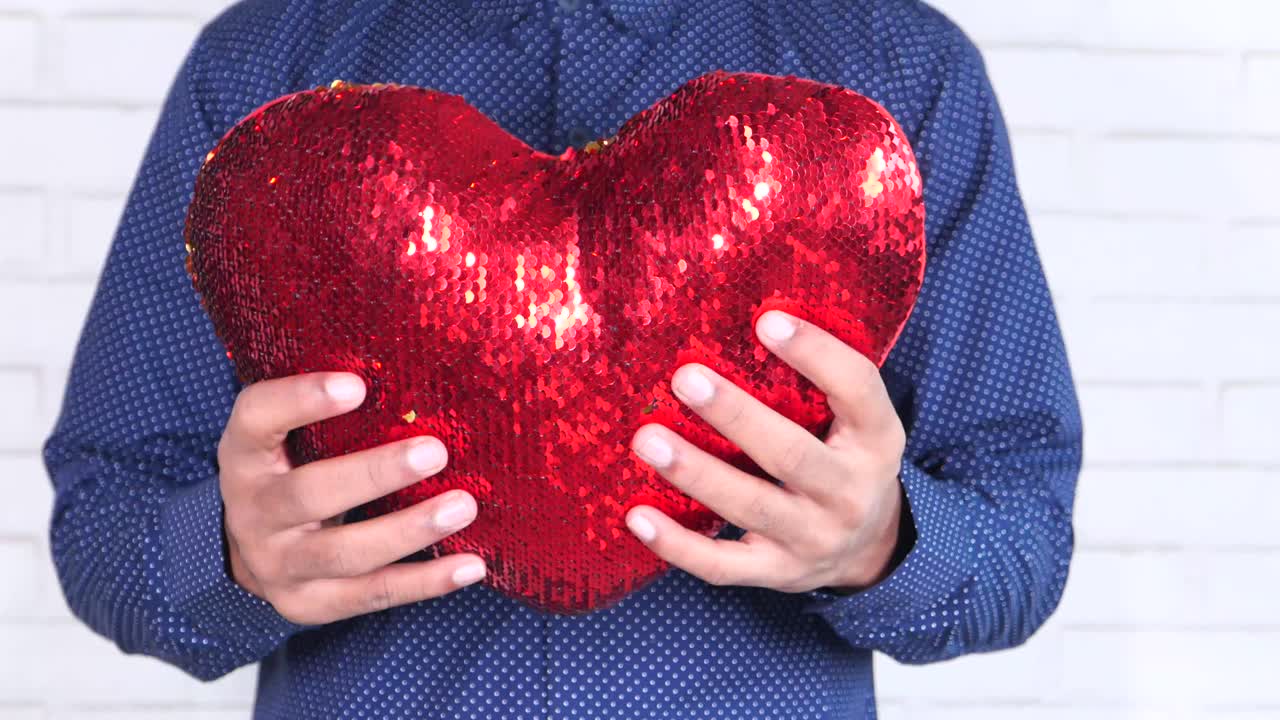 빨간색 세킨 심장 모양의 베개를 들고 있는 사람