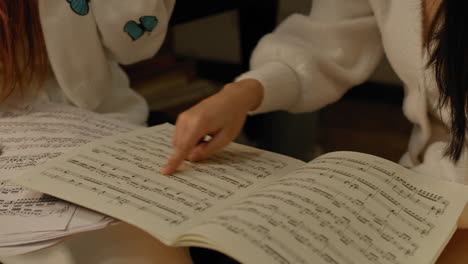 Two-girls-study-music-score-books,-pointing-out-details-with-fingers