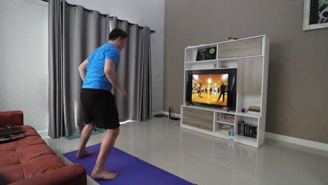 a chobby man in his 30s is working out in his living room in front of television , while following a fitness program moves