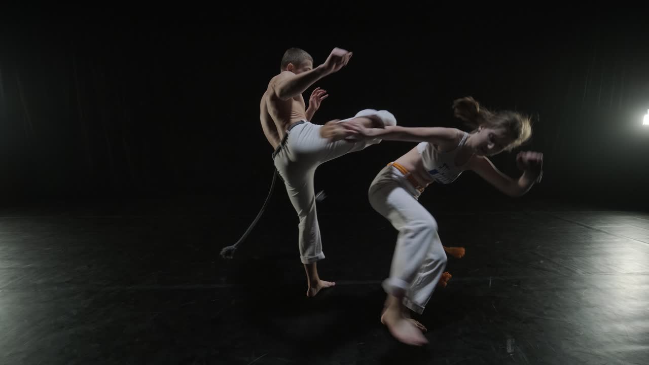 un grupo de bailarines profesionales están practicando capoeira en la oscuridad contra un foco de luz en un fondo negro de estudio. arte marcial afro-brasileño que combina elementos de la danza.
