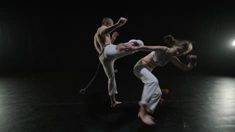 group of a professional dancers are practicing capoeira in darkness against a spotlight on a black background of studio. afro-brazilian martial art that combine elements of dance.