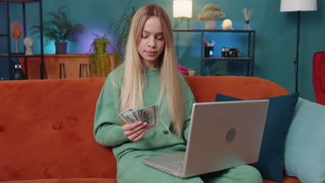 Smiling-young-woman-counting-money-cash-and-use-laptop-pc-calculate-domestic-income-earnings-at-home