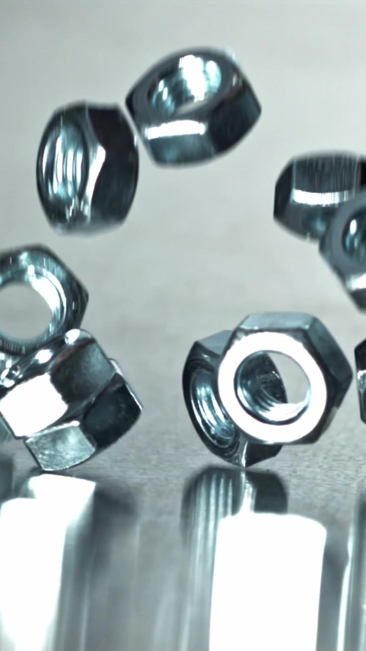 Porcas metálicas hexagonais caindo em câmera lenta em uma superfície brilhante