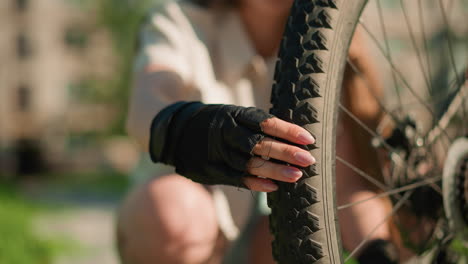 close-up of a rear bicycle tire with rugged tread, inspected for air pressure by person wearing black gloves, fingers pressing firmly continues pumping, background blurred for focus on tire and glove