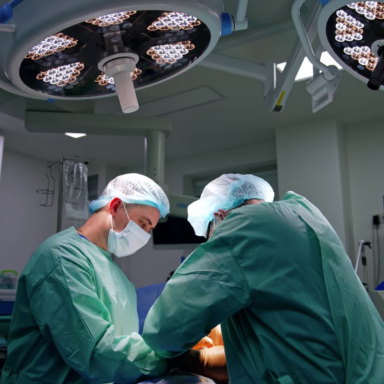To kirurger arbejder under en ortopædisk operation. Overkirurgen anvender et værktøj med ryggen mod kameraet.