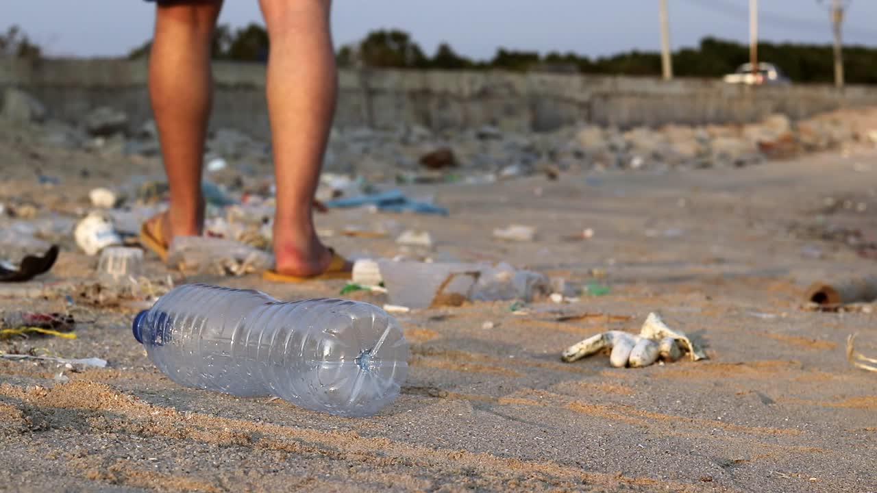 un turista blanco tira una botella de plástico en una playa de arena