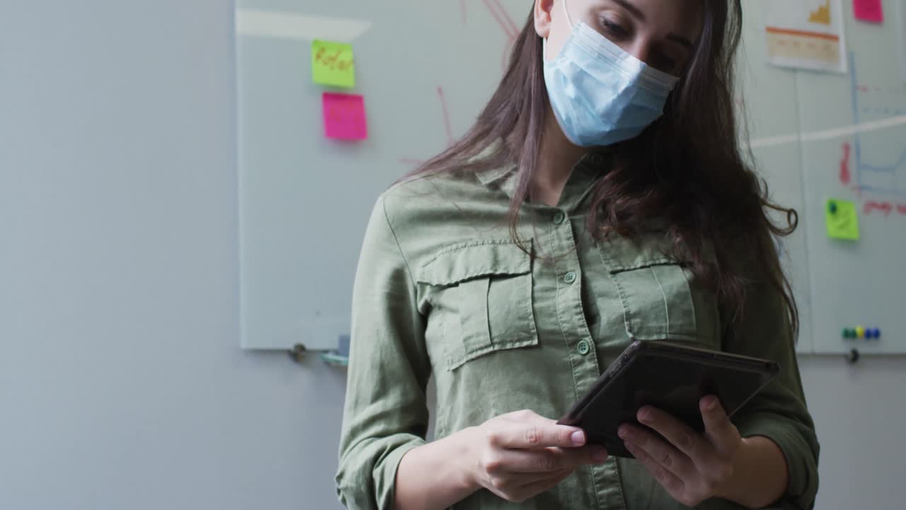 mujer de negocios caucásica en la sala de reuniones usando una máscara usando una tableta