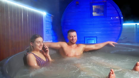 happy relaxed caucasian couple sit in the hot tub. smiling resting people in spa. woman speaks on the phone.
