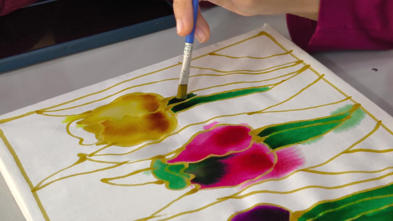 Nærbilde av et barn som maler fargerikt fargestoff på et tradisjonelt malaysisk batik-lerret. Ung student lærer kulturarvshåndverk gjennom praktisk kunst. Pedagogisk aktivitet som introduserer autentisk folkehåndverk.