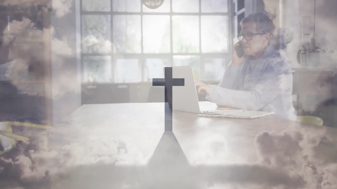 Animation overlay of cross and clouds on person working on laptop at school desk