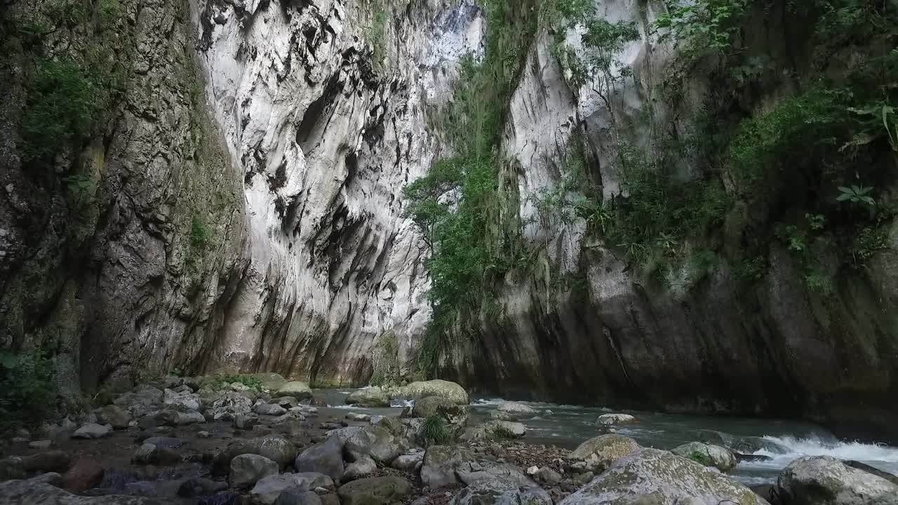 Crane and tilt down Las Puertas de Miraflores, a crevice with a narrow river at the bottom. Daytime, bright.