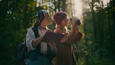 female friends with book and binocular exploring woods