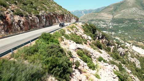 Albania,-cars-driving-on-a-treacherous-road-along-a-steep-mountain-slope,-aerial-view-from-a-drone