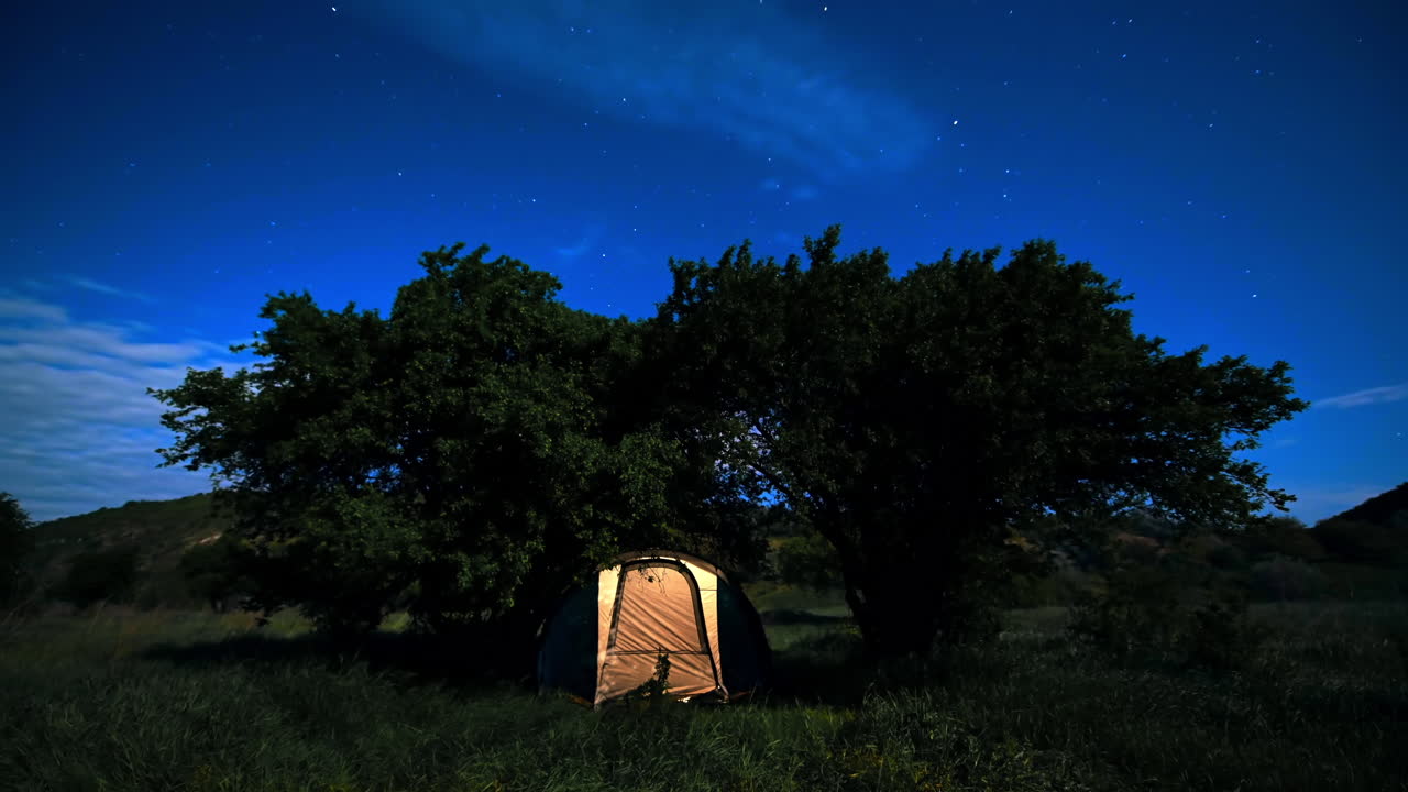 Vista timelapse di una tenda con luce all'interno nella natura di notte. Nuvole in movimento, cielo scuro