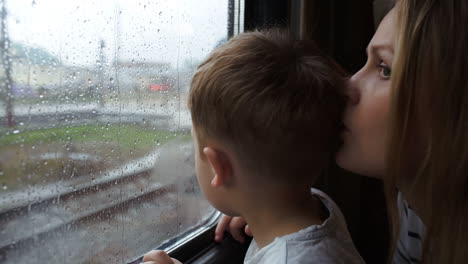 niño y su madre mirando por la ventana del tren mientras llueve