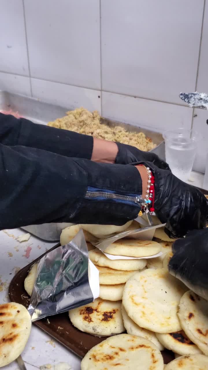Primer plano que captura el proceso detallado de preparar y rellenar una arepa recién hecha con sabrosa carne desmechada.