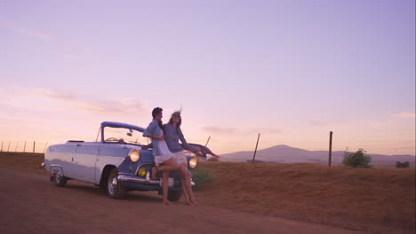 beautiful girl friends taking selfies on road trip at sunset with vintage car