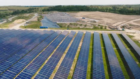 forward motion in solar panels seen from a drone with a landfill in the background, trucks transporting waste to landfill