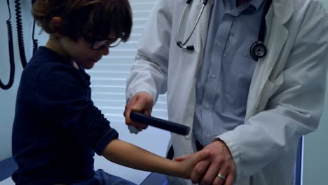 Young-asian-male-doctor-examining-a-caucasian-boy-patient-with-medical-tool-in-clinic-4k
