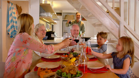 familia caucásica de varias generaciones brindando copas de bebidas en la mesa de comedor en casa 4k