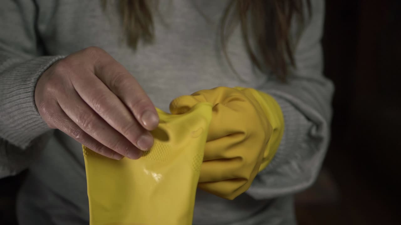 Woman's hands putting on yellow rubber gloves medium shot