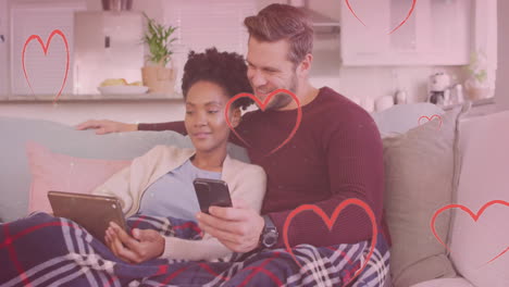 animación de corazones y puntos de luz sobre pareja diversa usando teléfono inteligente y tableta en el sofá