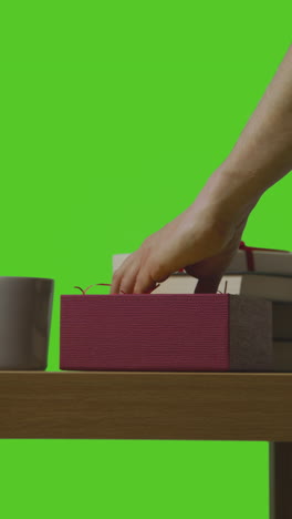 video vertical de un hombre poniendo un regalo en una caja envuelta en una mesa disparado contra una pantalla verde