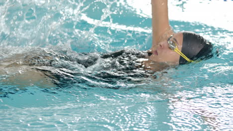 swimming backstroke in pool, woman wearing swim cap and goggles